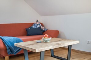 Una habitación con una mesa de madera, un frutero con fruta, una manta azul y un sofá rojo.
