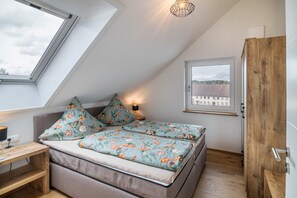 A bedroom with a skylight, a bed with floral bedding, a bedside table, and a view of buildings through a window.
