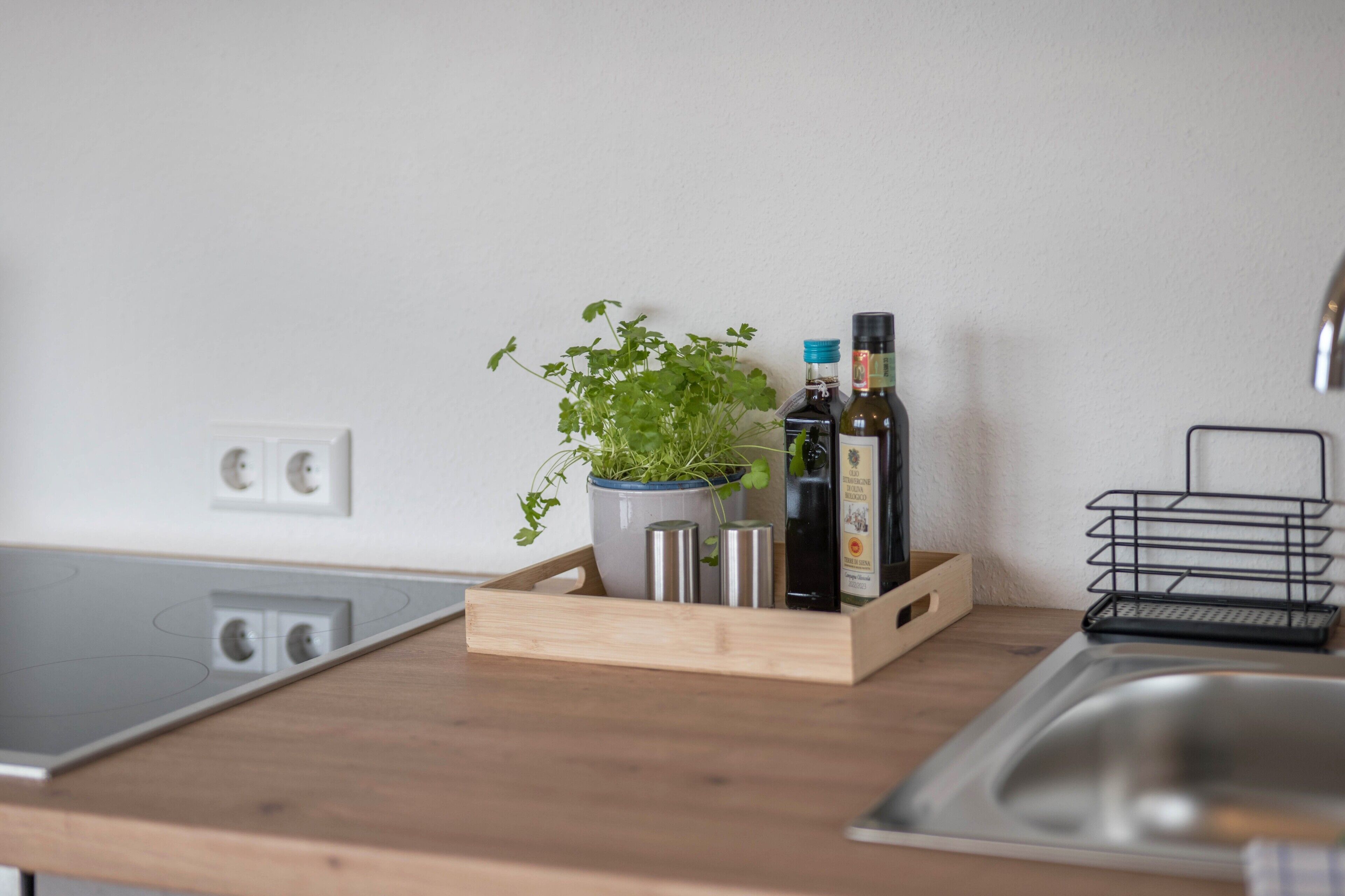 A kitchen with a wooden countertop, a potted plant, a bottle of olive oil, and a metal rack.