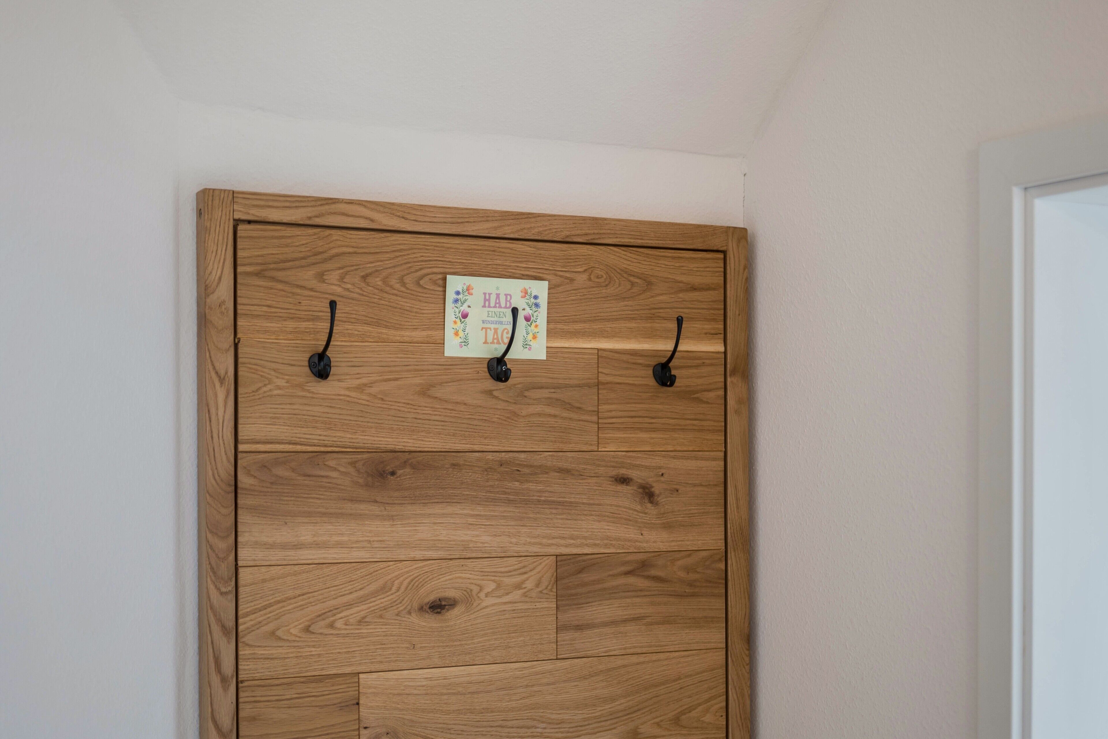 A wooden wardrobe with three black hooks and a small decorative sign.
