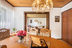 A dining area with a wooden table, chairs, a vase with flowers, a candle, and a chandelier. - Holiday Home 'Ferienwohnung Loy' with Private Terrace, Private Garden and Wi-Fi (Rastede)