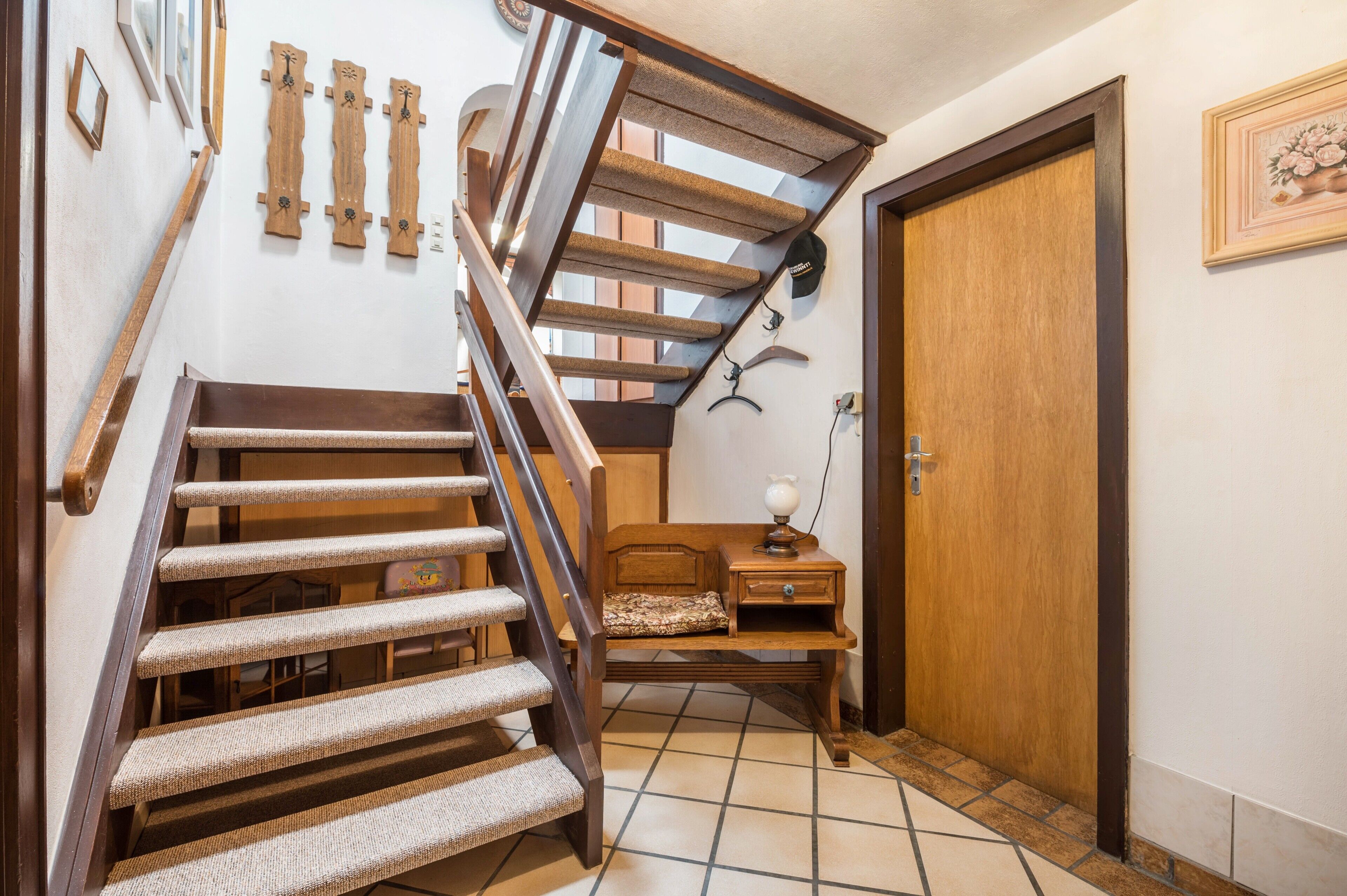 Un escalier en bois doté d’une main courante rembourrée, un petit banc en bois et une porte ornée d’un cadre.