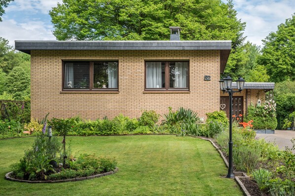 A single-story brick house with a well-maintained lawn, a small garden, and a visible number '2' on the front door.