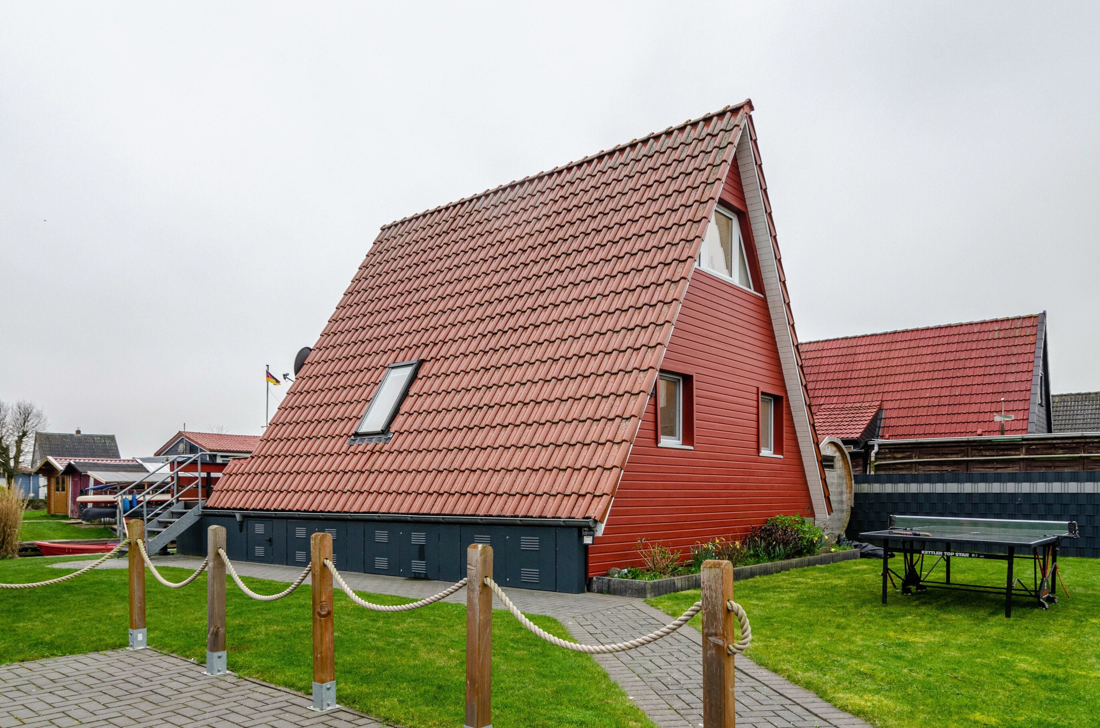 En byggnad med rött tak och ett sluttande tak, en trappa som leder till en dörr och ett stängsel av sammanlänkade kedjor i förgrunden.