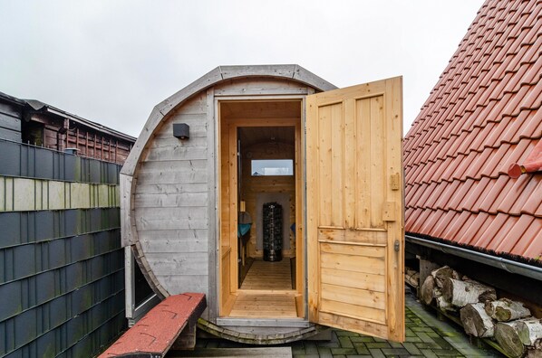 A wooden structure with an open door, a small bench, and a log storage area.