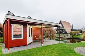 A red building with a covered patio, a small boat, and a pond.