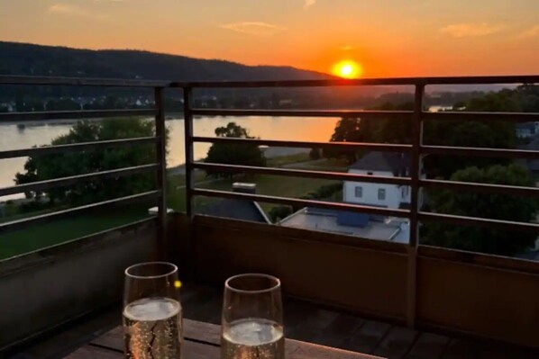 A balcony with a view of a sunset over a river and buildings.