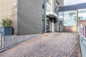 A modern building with a brick pathway, metal railings, and a potted plant.