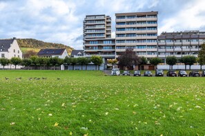 A grassy field with a row of parked cars and a building with multiple floors in the background.