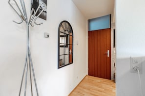 A hallway with a wooden door, a window with a black frame, and a wall-mounted light fixture.