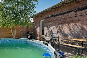 En swimmingpool med en kant av kakel, en mur av tegelsten, träbänkar och en stege.