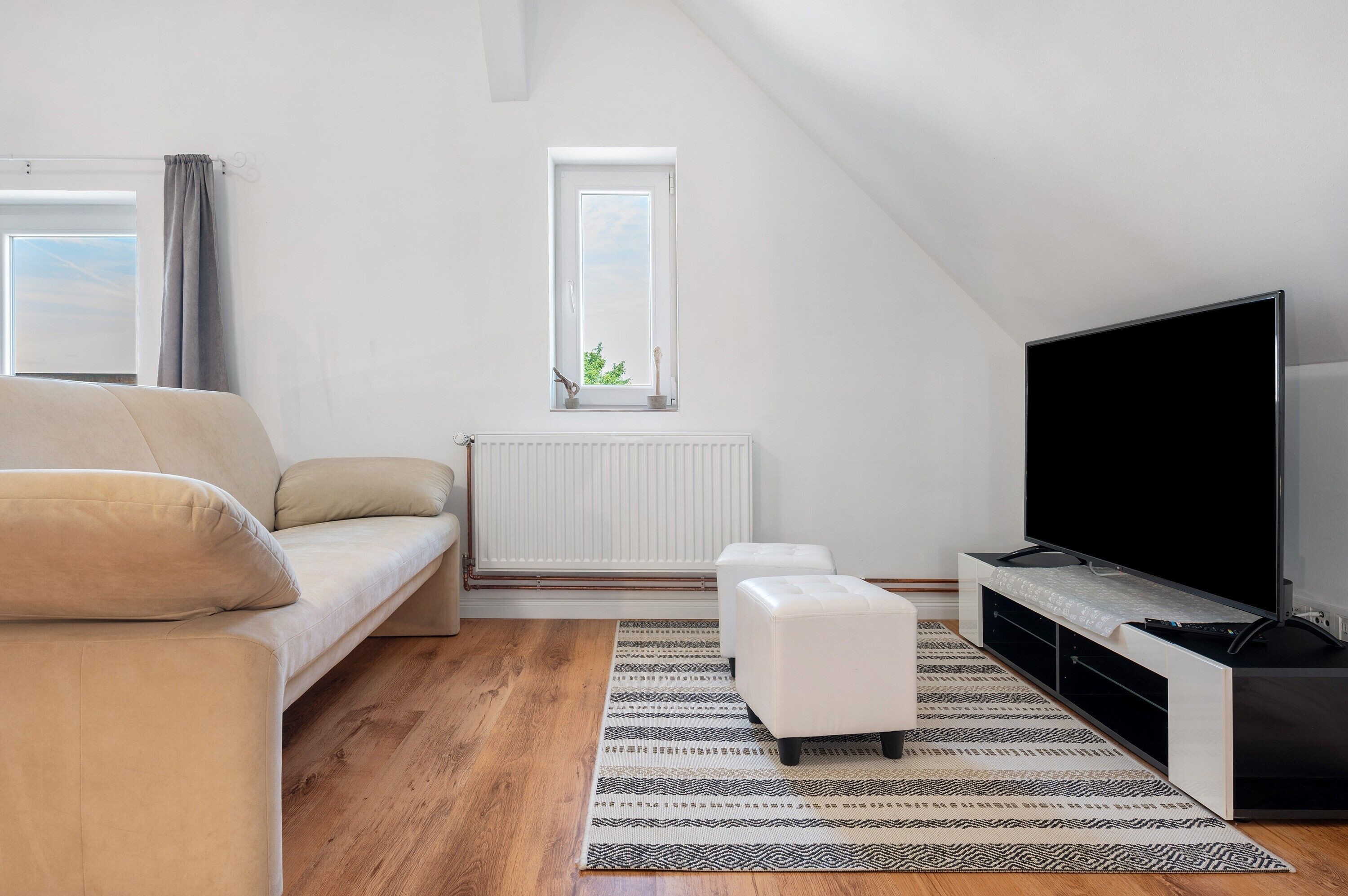 Una sala de estar moderna con sofá, reposapiés, televisor y ventana con vistas.