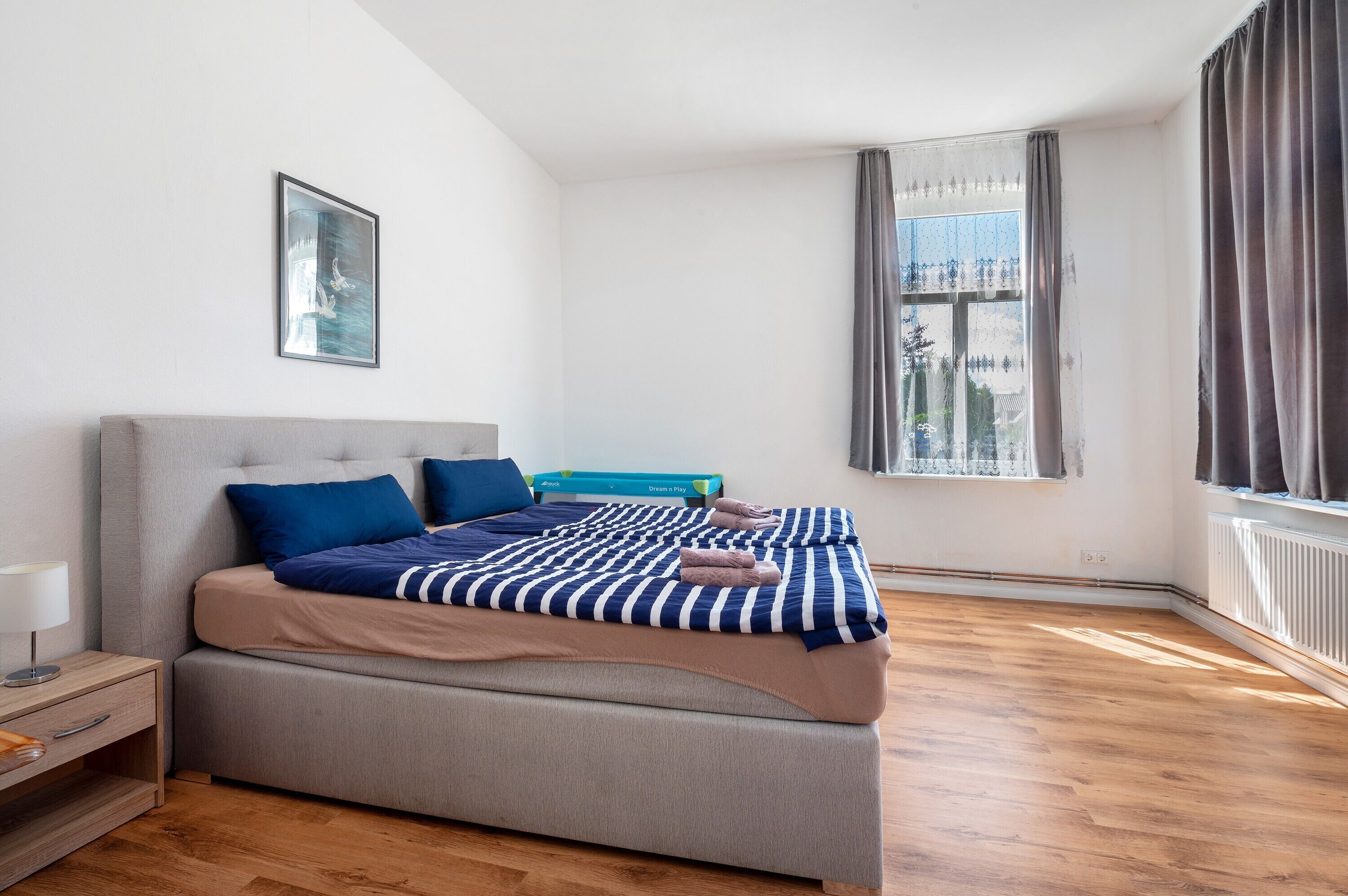 Une chambre à coucher avec un lit, une table de chevet, une fenêtre avec des rideaux et une vue sur un bâtiment à l’extérieur.