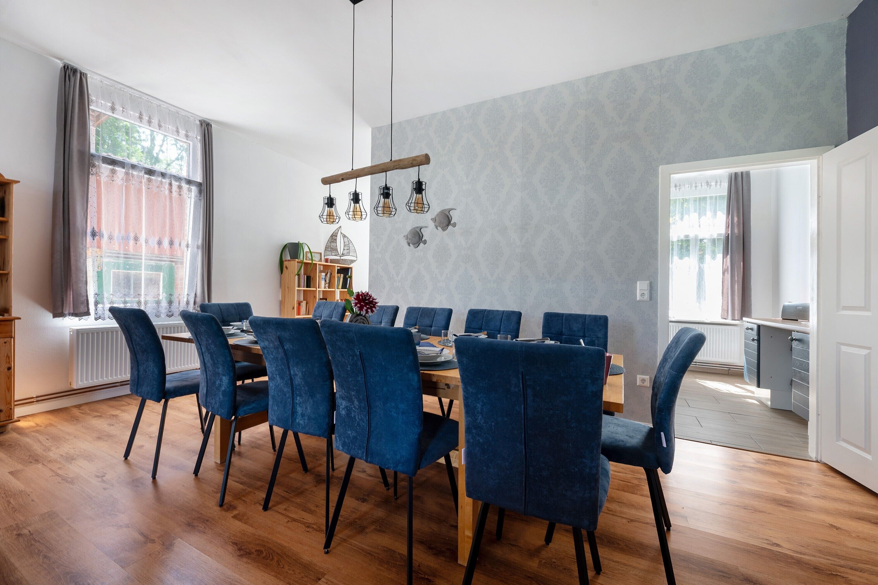 Un coin repas avec une table en bois et des chaises bleues, une bibliothèque et une fenêtre avec des rideaux.