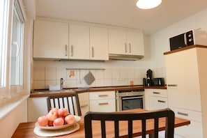 A kitchen with white cabinets, a wooden table with a plate of apples, a microwave, and an oven.