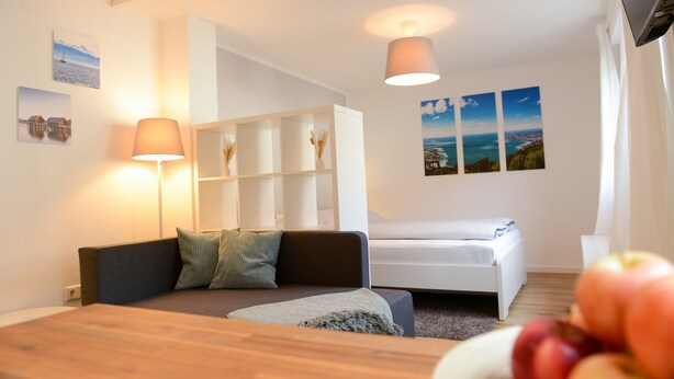 Ein modernes Zimmer mit Bett, einer Schlafcouch, einem Holztisch und einem weißen Kleiderschrank.