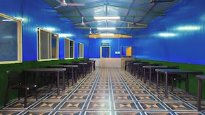 A room with blue walls, green borders, and patterned flooring. There are tables and chairs arranged in rows. - Rudra Adventures (Narendranagar)
