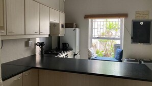 Uma cozinha com armários, fogão, geladeira e janela com vista para vegetação.