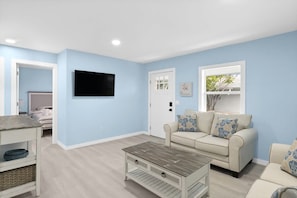 Un salón con una pared azul claro, un sofá color beige, una mesa de centro y un televisor montado en la pared.