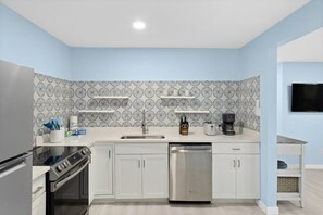 A modern kitchen with white cabinets, a stainless steel dishwasher, a built-in oven, and a coffee maker on the countertop.