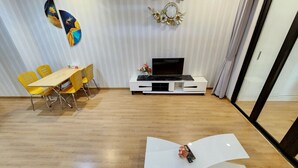 Un salon moderne avec un coin repas, doté d’un parquet, de chaises jaunes, d’une table blanche, d’un téléviseur à écran plat et d’œuvres d’art décoratives murales.