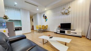 Un salon moderne avec un canapé en cuir noir, des tables basses blanches, un téléviseur à écran plat et un coin repas avec des chaises jaunes.