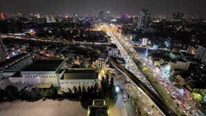 Une vue aérienne d’une ville de nuit, avec des bâtiments illuminés, des rues animées et, au premier plan, un bâtiment remarquable surmonté d’un toit végétalisé.