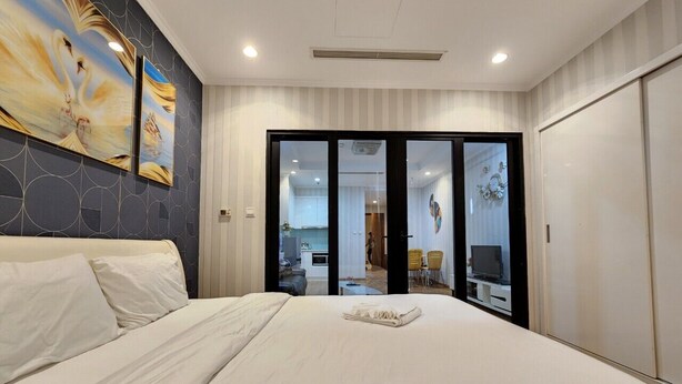 Une chambre d’hôtel moderne avec un grand lit, une vue sur la cuisine et l’espace de vie grâce à une porte vitrée, et un tableau accroché au mur.