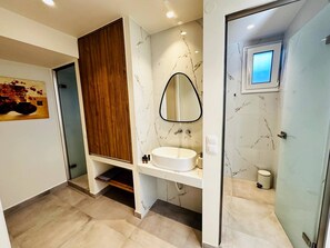 A modern bathroom with a marble vanity, a wooden cabinet, a freestanding mirror, and a small window.