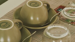 A table with two ceramic cups, a glass jar, and a metal kettle.