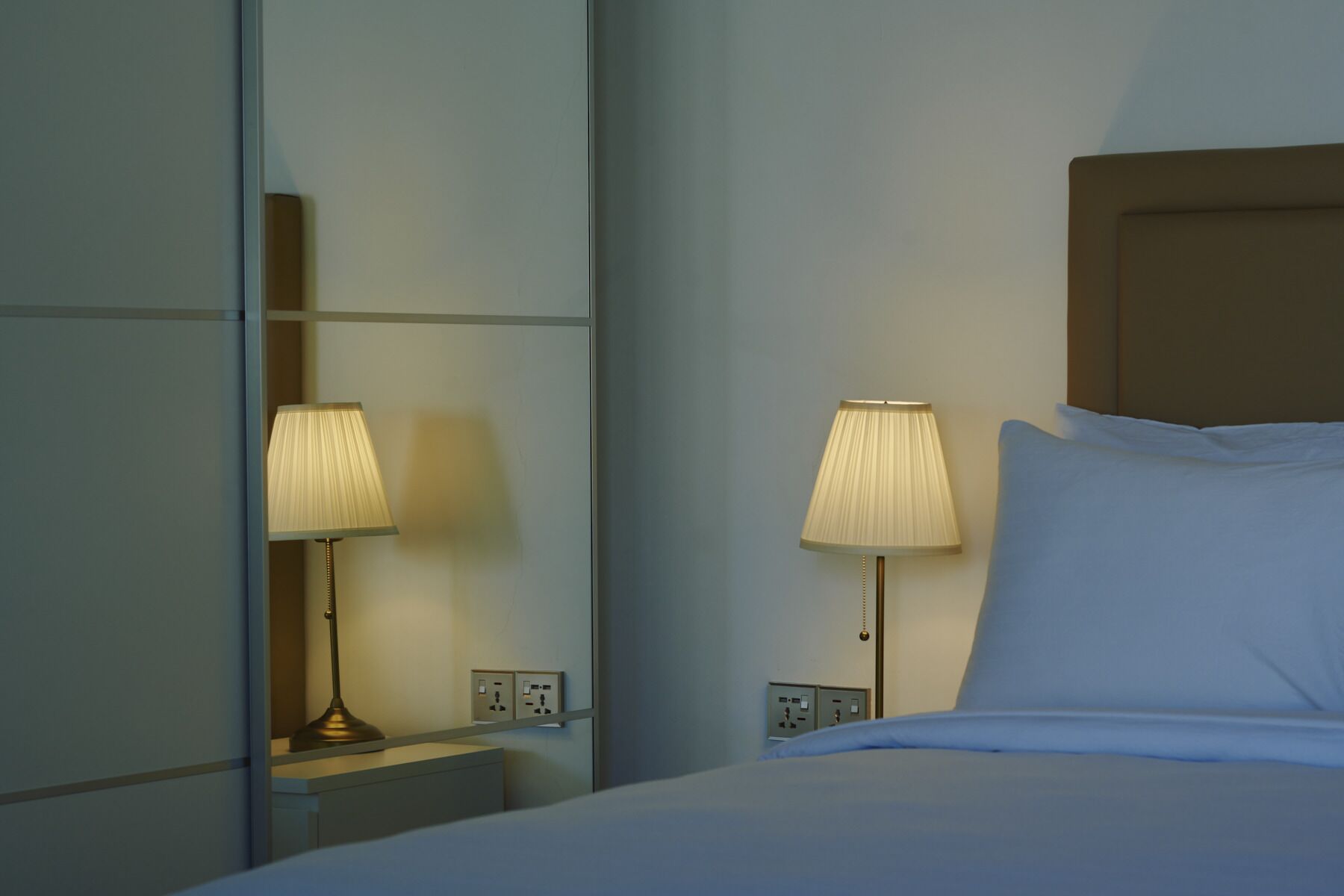 A hotel room with a bed, two bedside lamps, a nightstand, and a mirror.