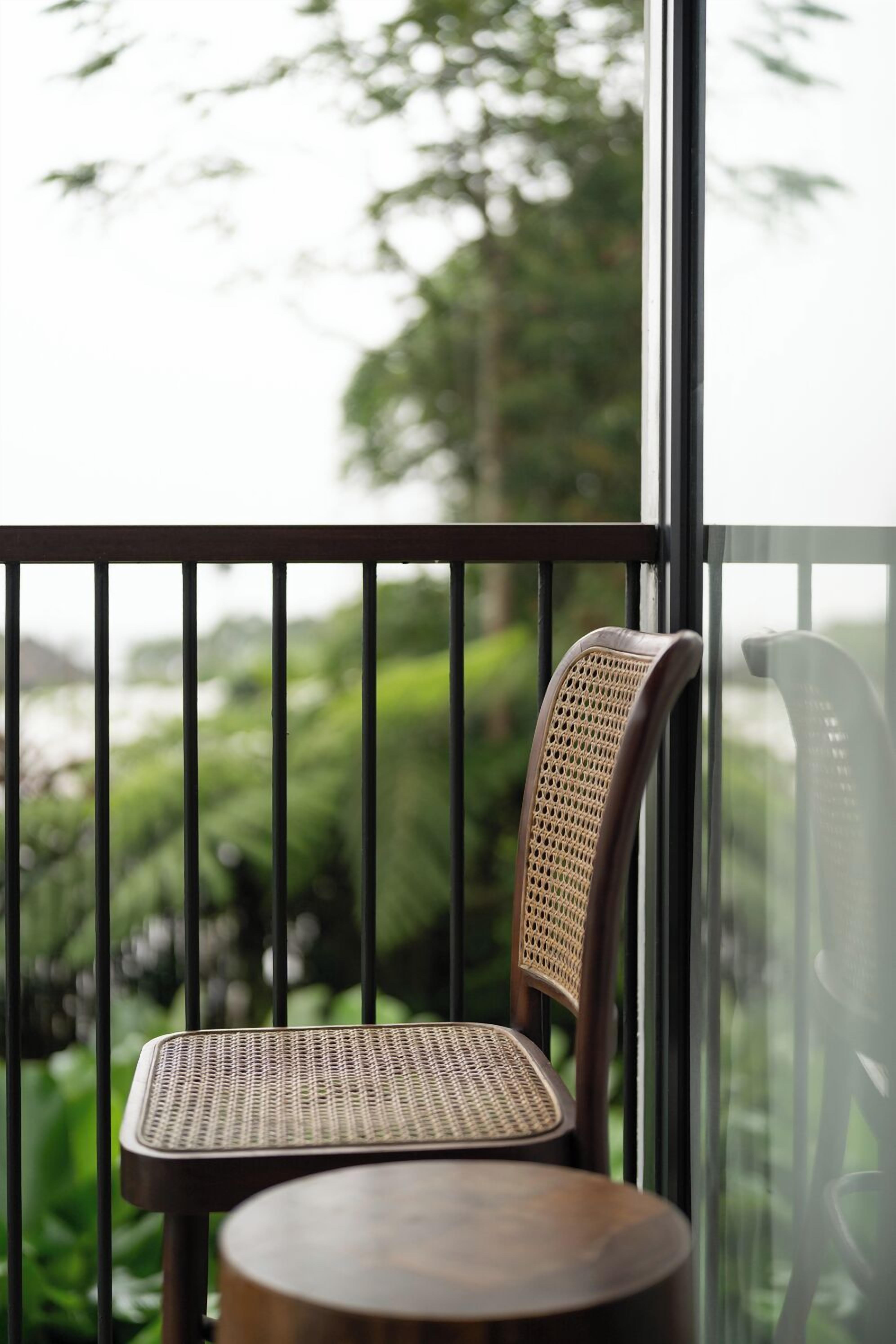 A balcony with a wicker chair and a small table, overlooking a lush green landscape.