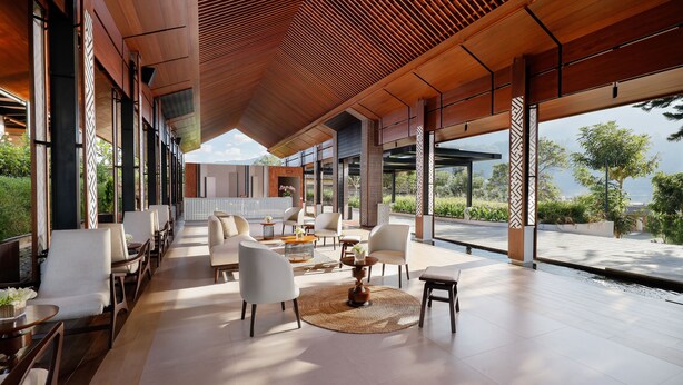 Un espace intérieur moderne doté d’une grande salle à manger, de chaises blanches et d’une table centrale surmontée d’un tapis tissé.