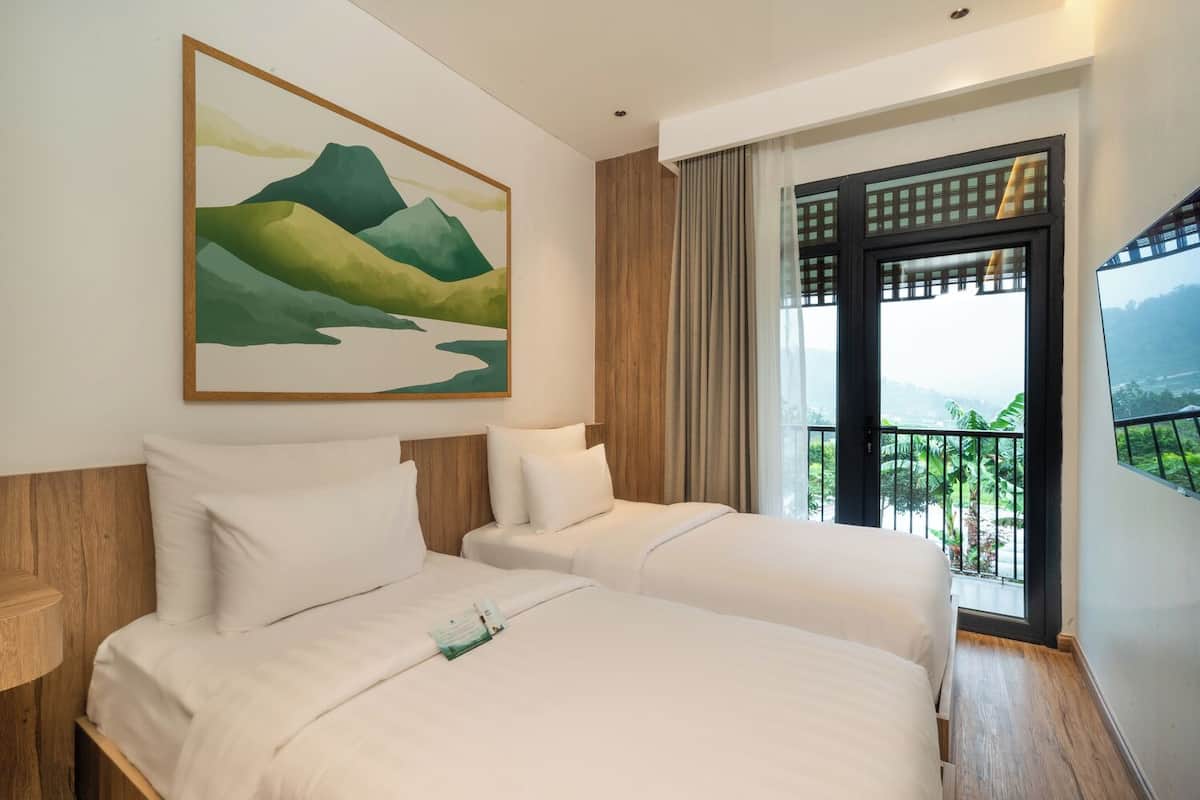 Habitación de hotel con dos camas, un cuadro de montañas, una ventana con vistas a la vegetación y un balcón con barandilla.