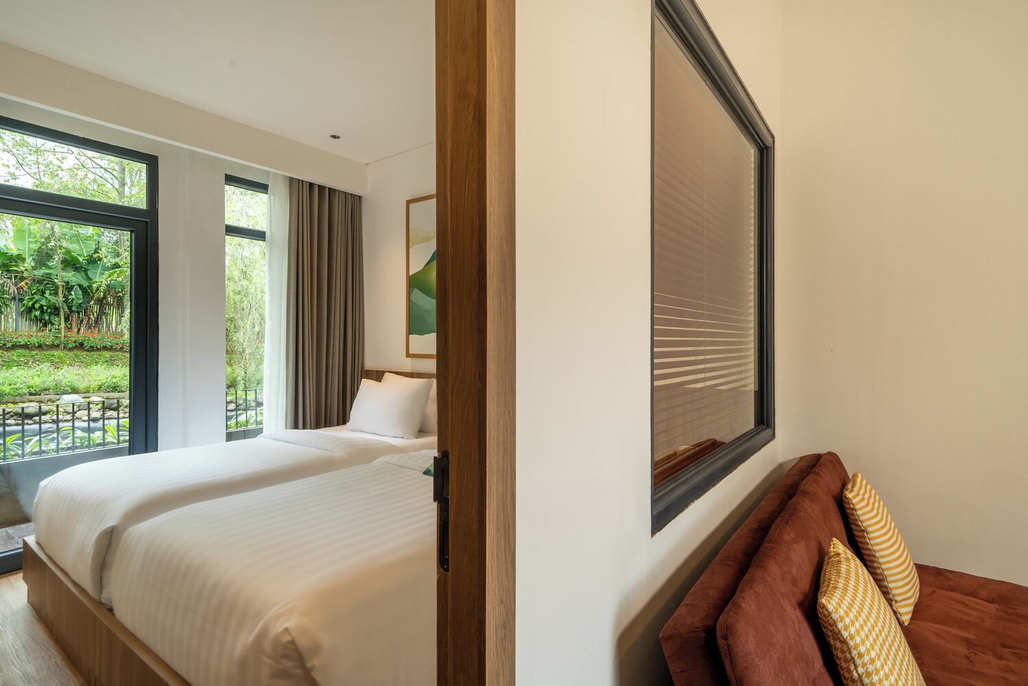 A hotel room with two beds, a large window, and a view of greenery outside.