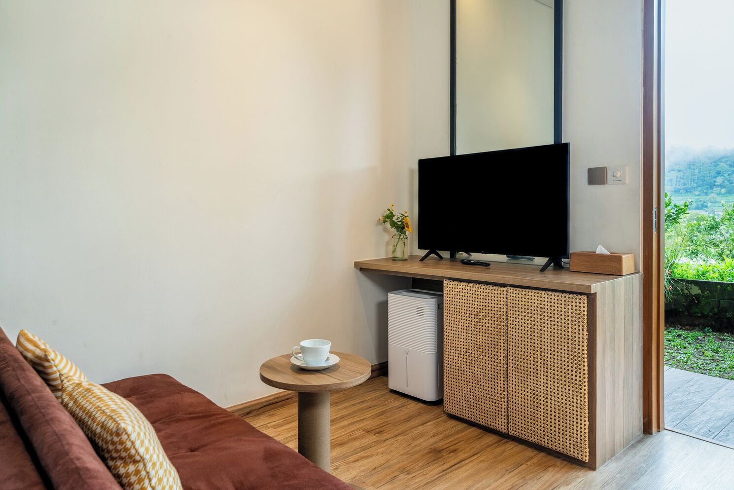 Ein modernes Zimmer mit Flachbildfernseher, einem kleinen Tisch mit Tasse, einer Couch und einem Rattankorpus.