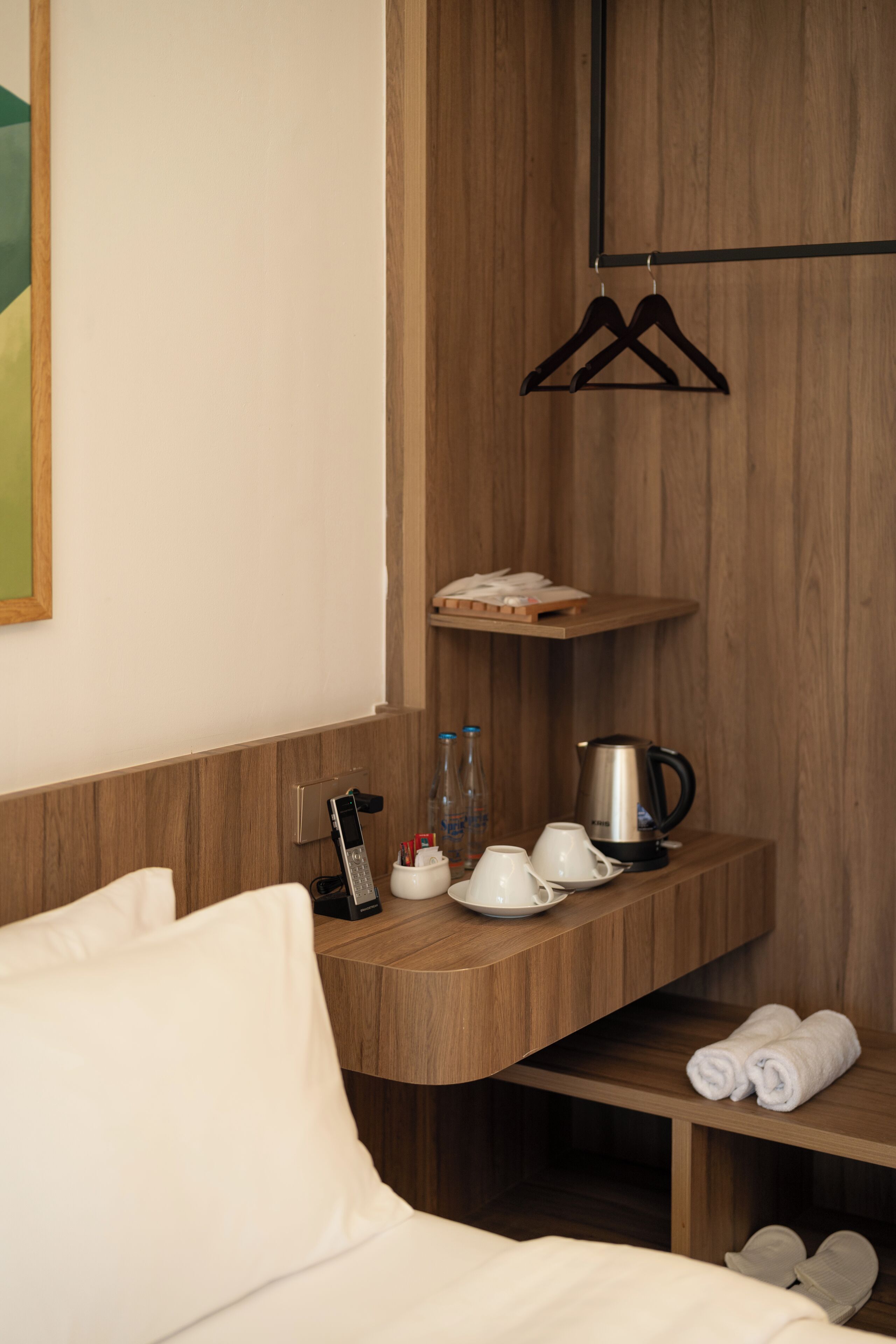 A hotel room with a wooden vanity, a bed, a shelf with toiletries, and a hanging rack.