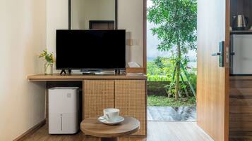 A modern room with a flat-screen TV on a wooden console, a small table with a cup, and a view of a garden through an open door.