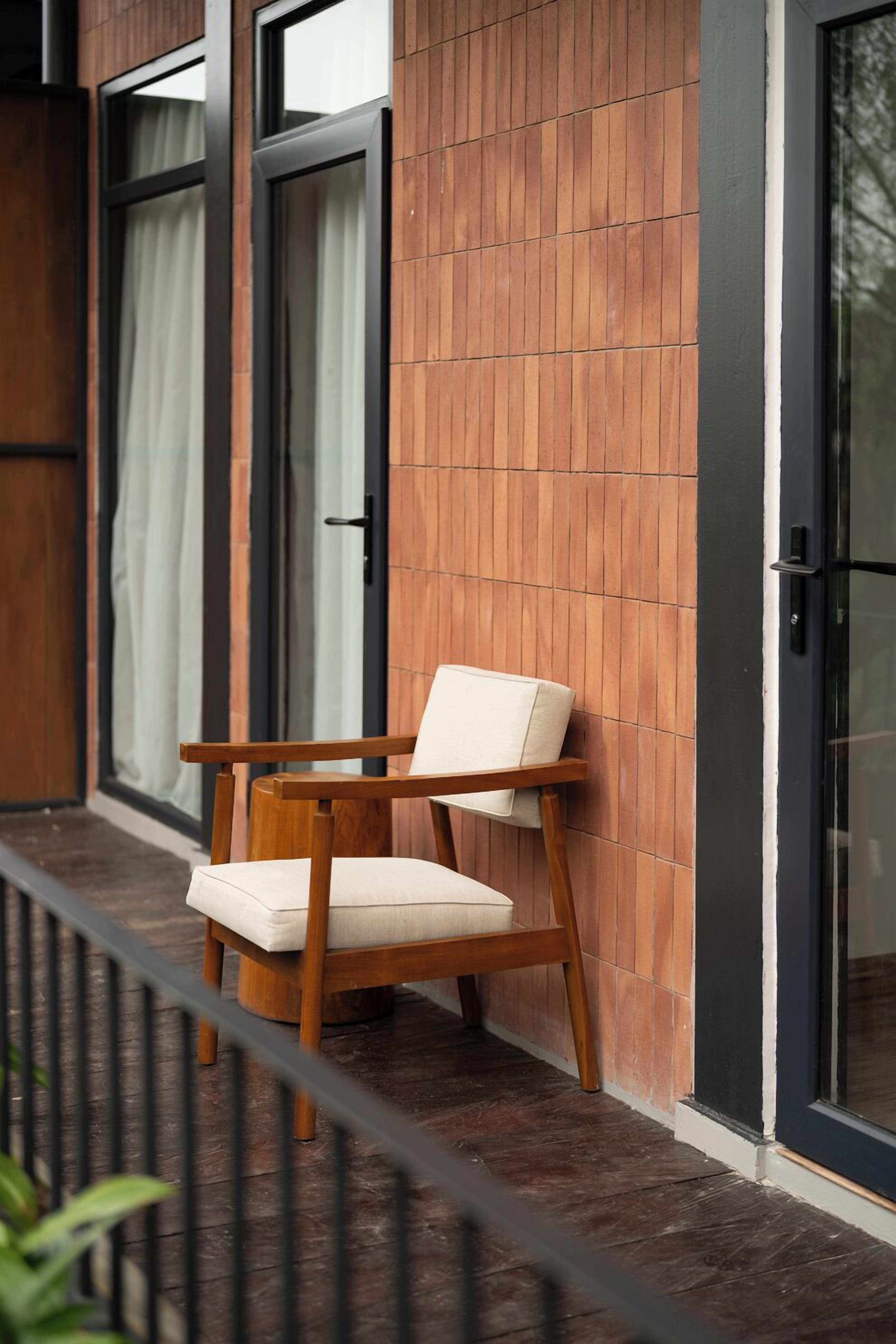 Una silla de madera con cojín, apoyada contra una pared con paneles de madera verticales y una puerta negra.