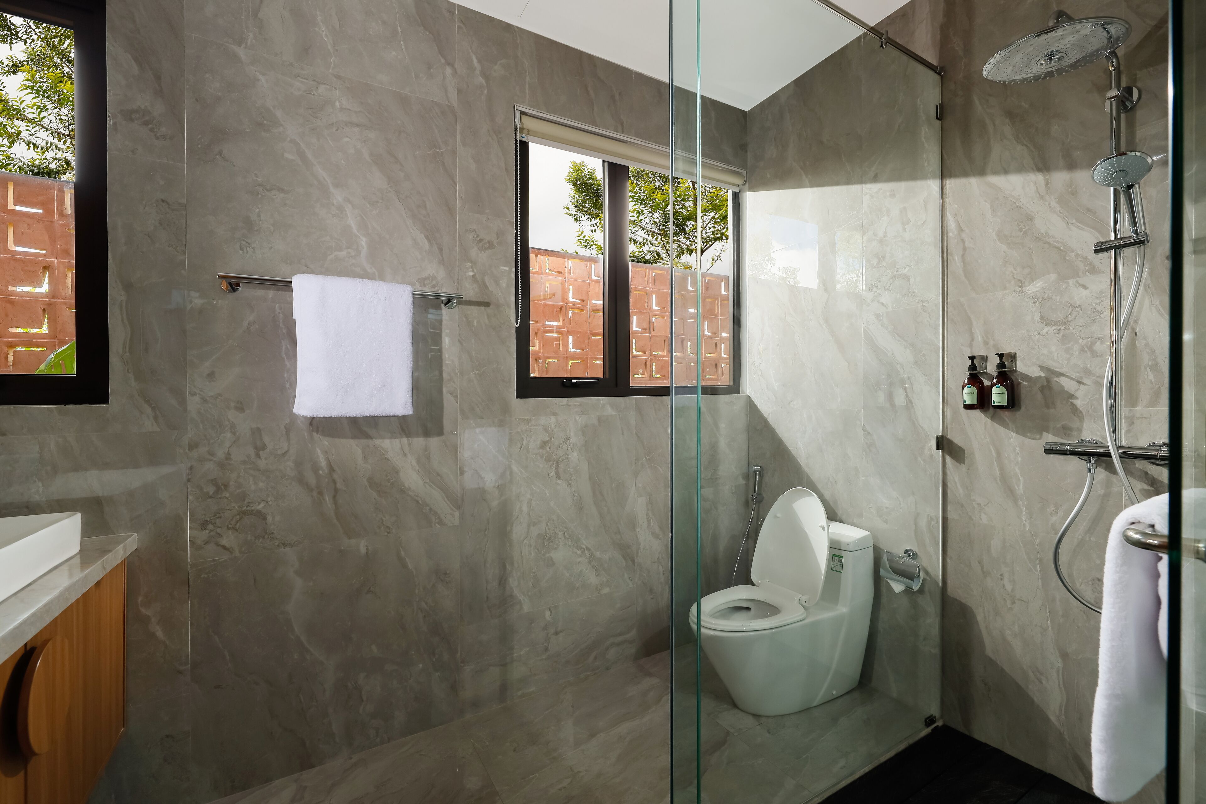A modern bathroom with a glass-enclosed shower, a toilet, and a sink with a marble countertop.