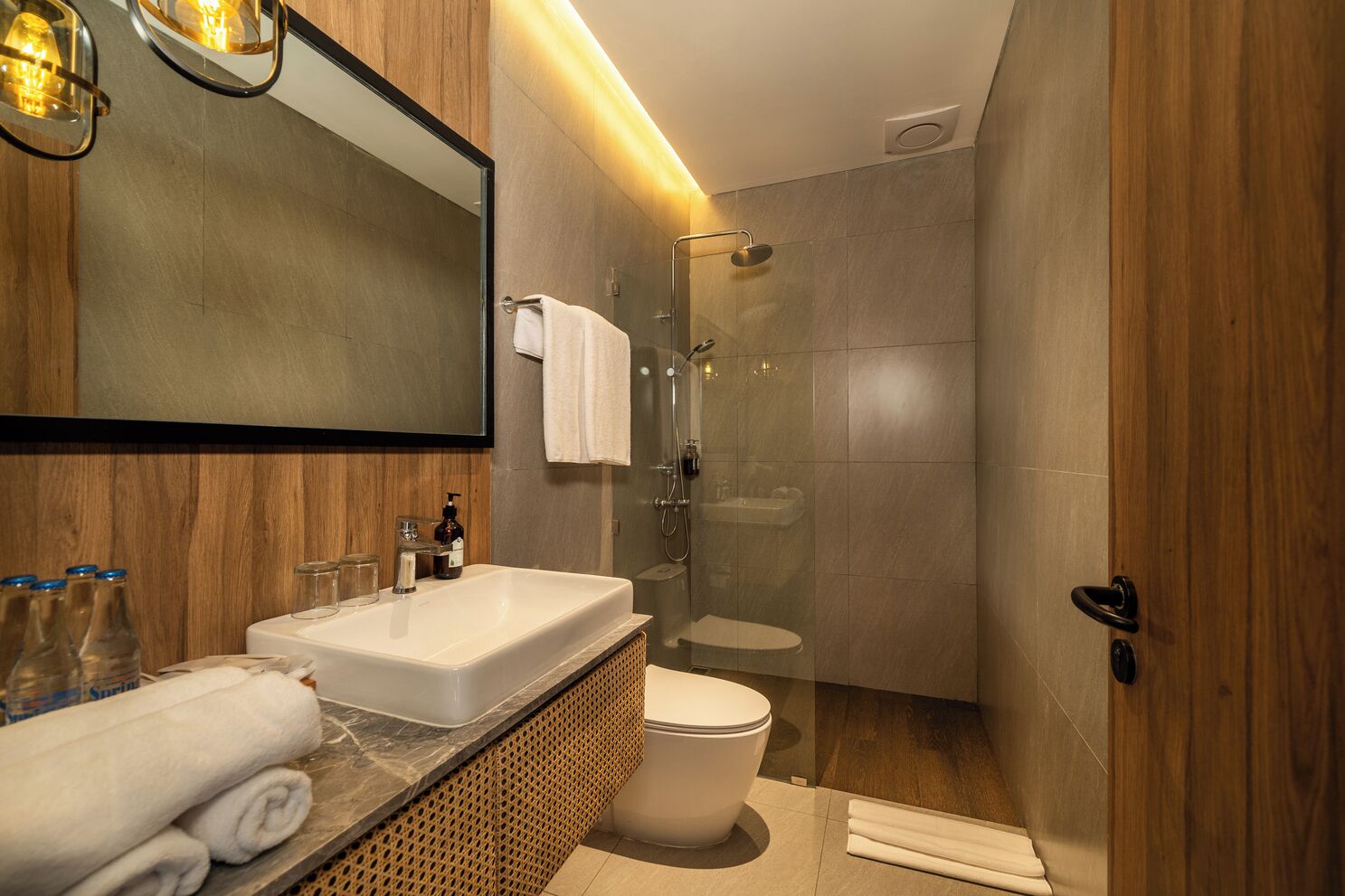 A modern bathroom with a large mirror, a sink, a toilet, and a glass-enclosed shower.