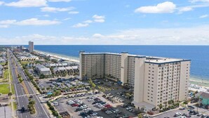 A multi-story hotel with a parking lot and a view of the beach.