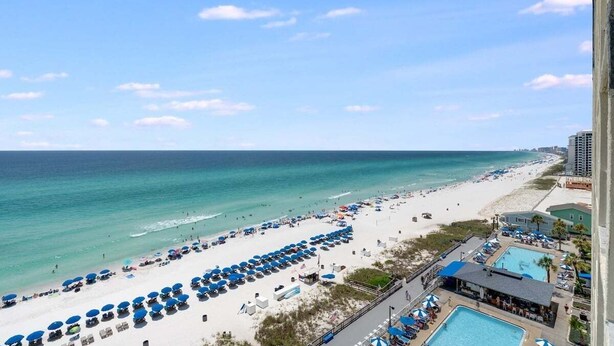 A beach resort with rows of sun umbrellas, a swimming pool, and a view of the ocean.