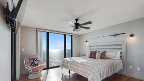 Un dormitorio con cama, una silla, ventilador de techo y vista al océano.