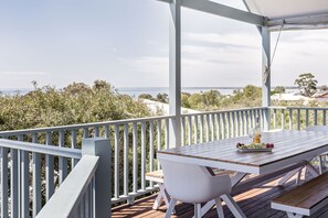 A covered outdoor seating area with a table and benches, overlooking a scenic view of the sea and greenery. - Seaview in Old Dunsborough: ocean views and pet friendly (Dunsborough)