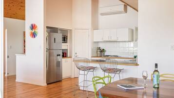 A modern kitchen with white cabinets, a stainless steel refrigerator, and a wooden dining table with colorful chairs.