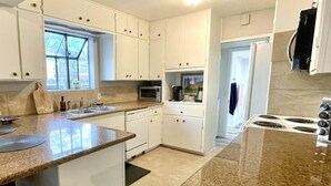 Cucina con mobili bianchi, un piano di lavoro in granito, un forno a microonde, un fornello e una finestra con vista sugli alberi.