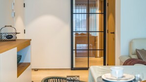 A modern room with a sliding door leading to a dining area, a wooden desk with a basket, and a sofa with a blanket. - Sol i Mar - located in the heart of Westende (Middelkerke)