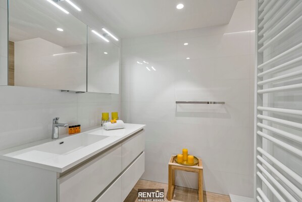 Un baño moderno con lavamanos, espejo y ducha blancos.
