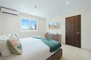 A bedroom with a bed, a dresser, a television, and a door. - Luxe Beach Condo Le Vent Townhouse 17 by Bocobay (Noord)